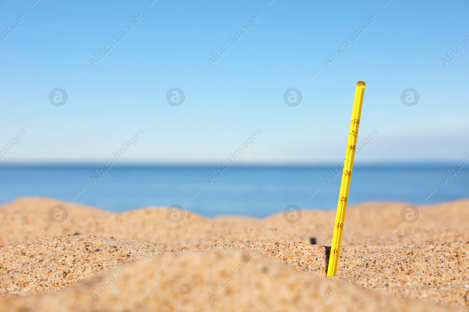 Photo of Yellow weather thermometer in sand near sea, space for text