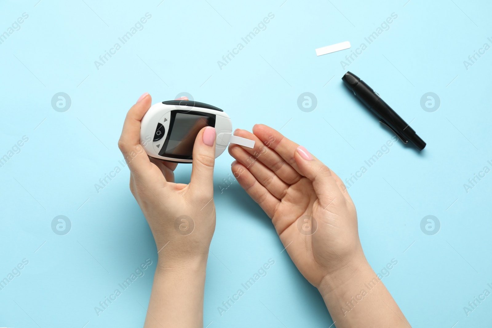 Photo of Diabetes. Woman checking blood sugar level with glucometer on light blue background, top view