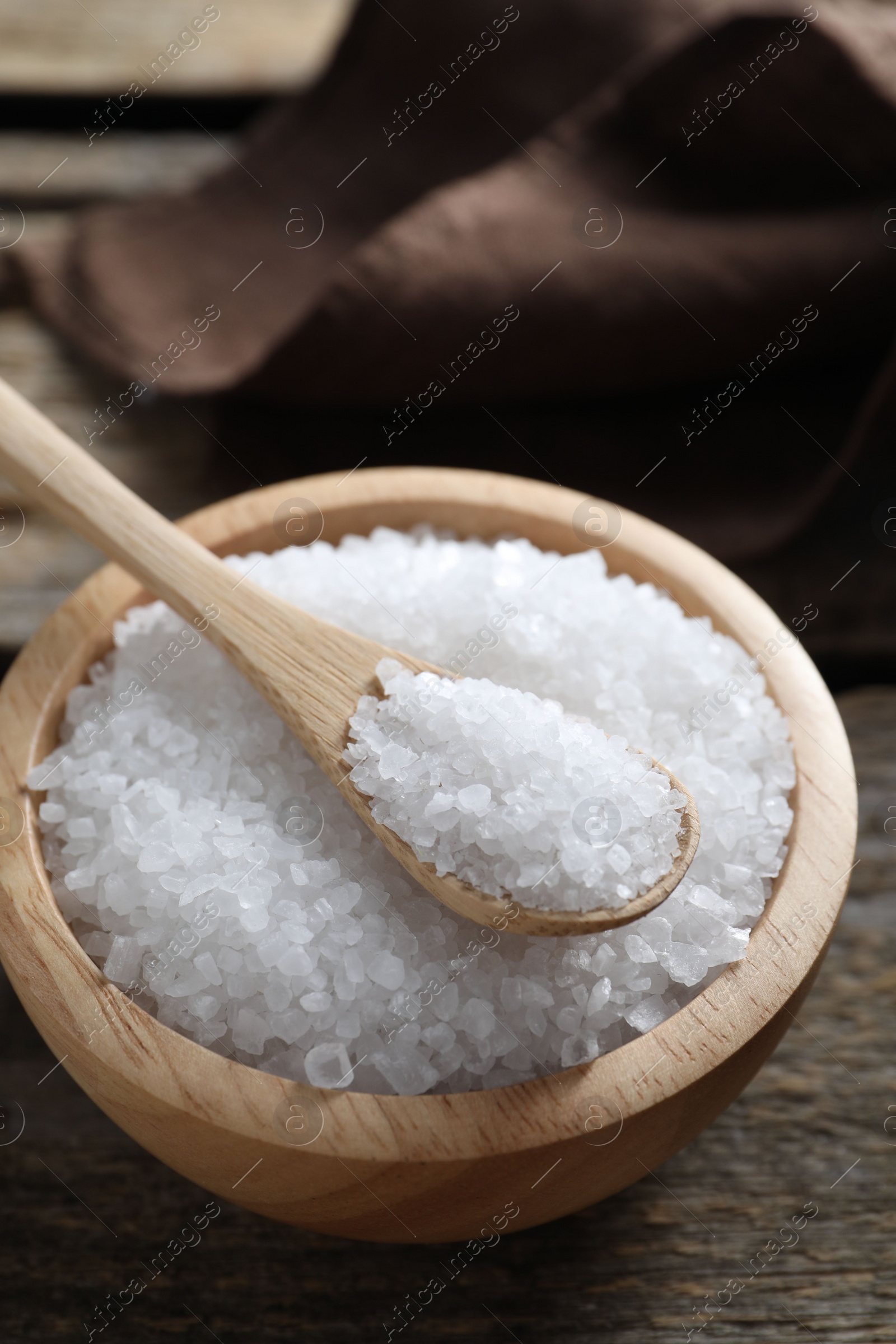 Photo of Organic salt in bowl and spoon on wooden table, closeup