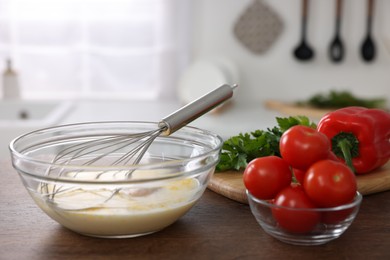 Photo of Whisk, bowl, beaten eggs and other ingredients on wooden table indoors