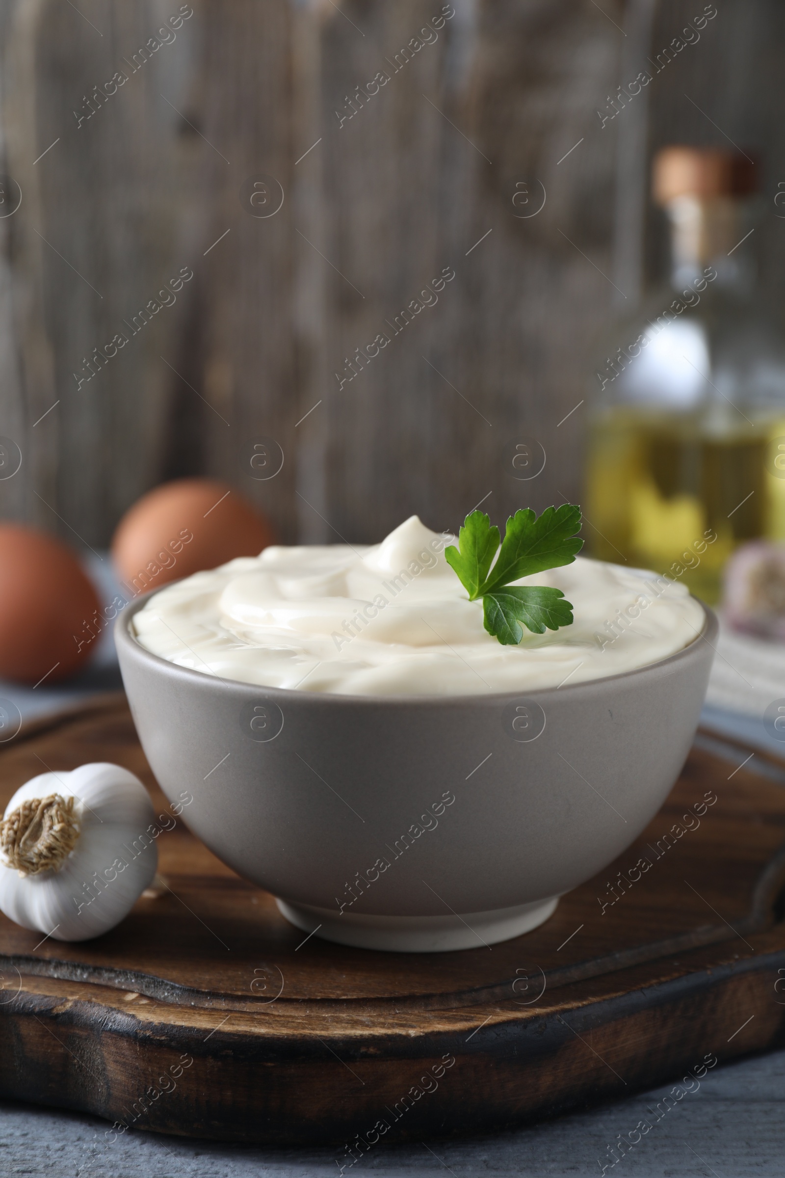 Photo of Tasty mayonnaise in bowl and garlic on light grey wooden table, closeup. Space for text