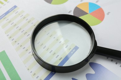 Photo of Magnifying glass on accounting documents with data and graphs, closeup