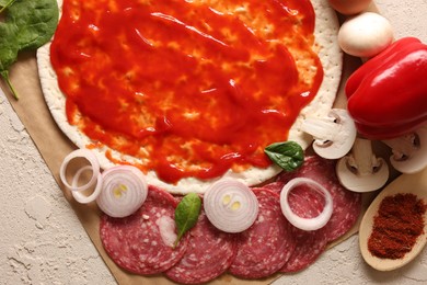 Pizza base smeared with tomato sauce and products on light textured table, top view