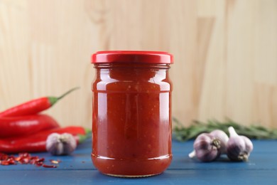 Photo of Spicy chili sauce in jar, garlic and peppers on blue wooden table