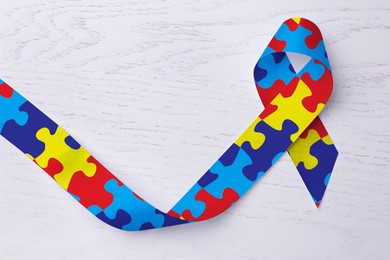 Image of World Autism Awareness Day. Colorful puzzle ribbon on white wooden background, top view
