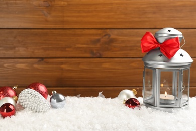 Photo of Christmas lantern with burning candle and festive decor on snow. Space for text