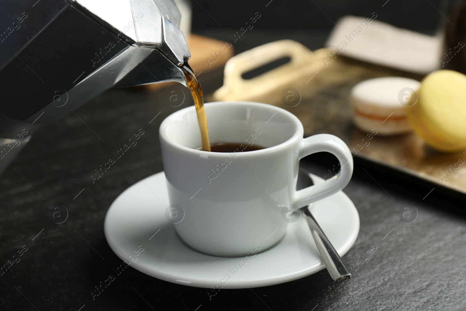 Photo of Pouring coffee from moka pot into cup at dark textured table, closeup