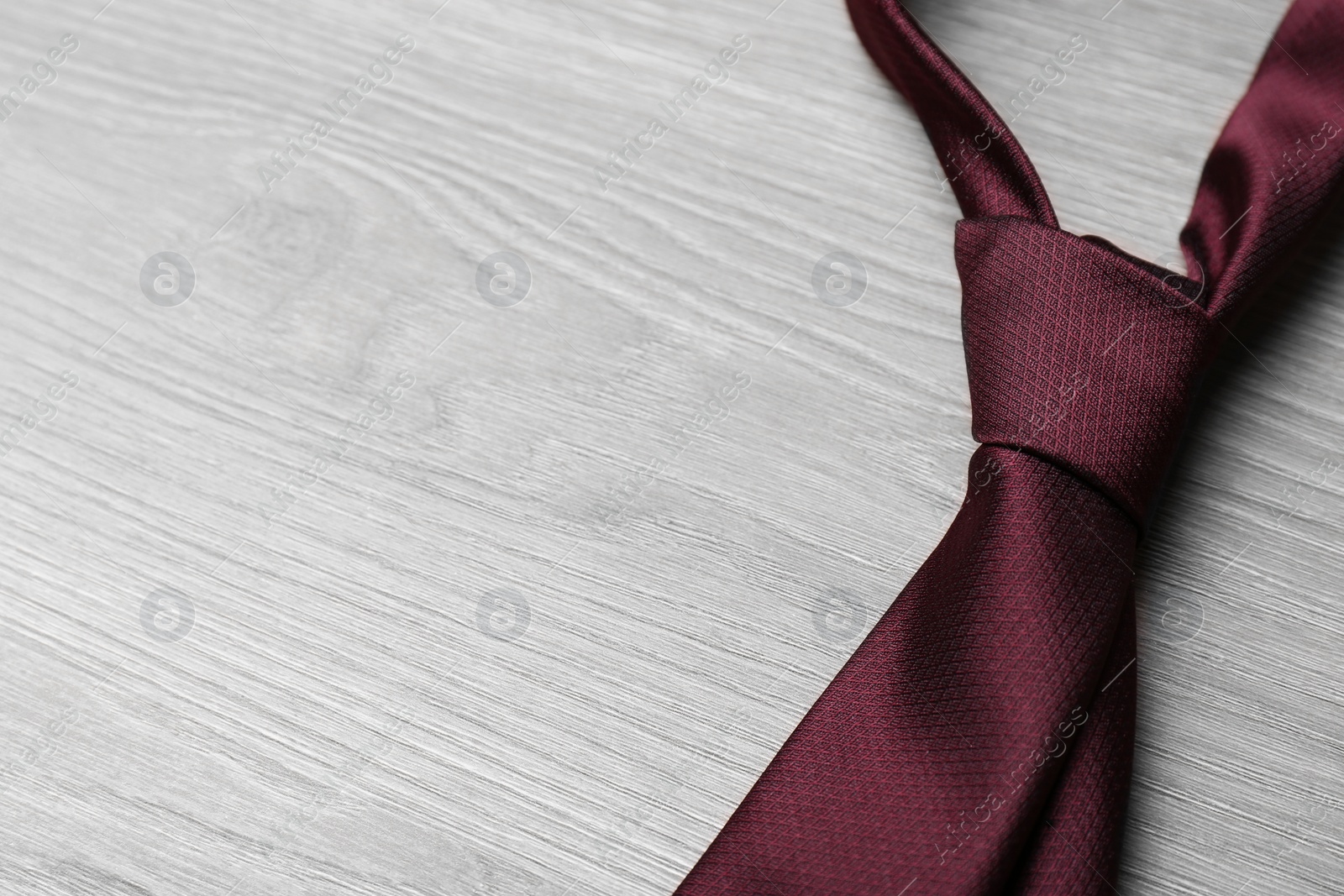 Photo of Stylish bordeaux necktie on grey wooden table, space for text