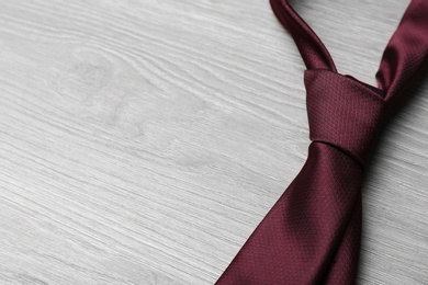 Photo of Stylish bordeaux necktie on grey wooden table, space for text