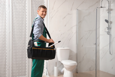 Photo of Professional plumber with toolbox near toilet bowl in bathroom