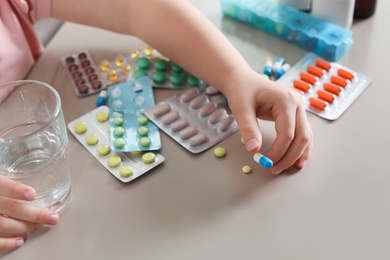 Photo of Little child with many different pills and water at table, closeup. Danger of medicament intoxication