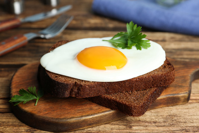 Photo of Tasty fried egg with parsley and rye bread on wooden board, closeup