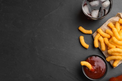 Photo of Crunchy cheesy corn snack, ketchup and cola on black table, flat lay. Space for text