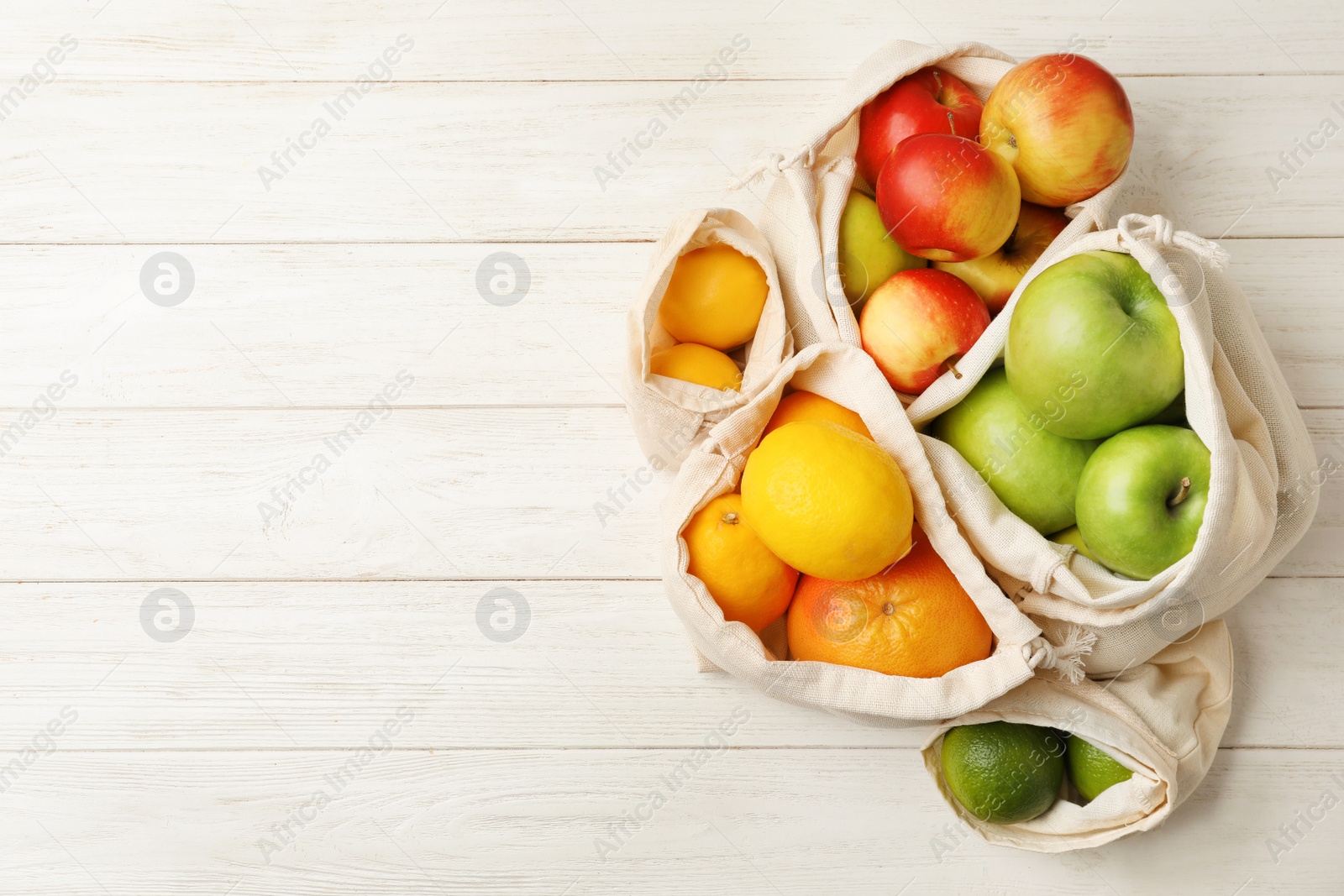 Photo of Cotton eco bags with fruits on white wooden table, flat lay. Space for text