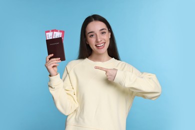 Happy woman pointing at passport and tickets on light blue background