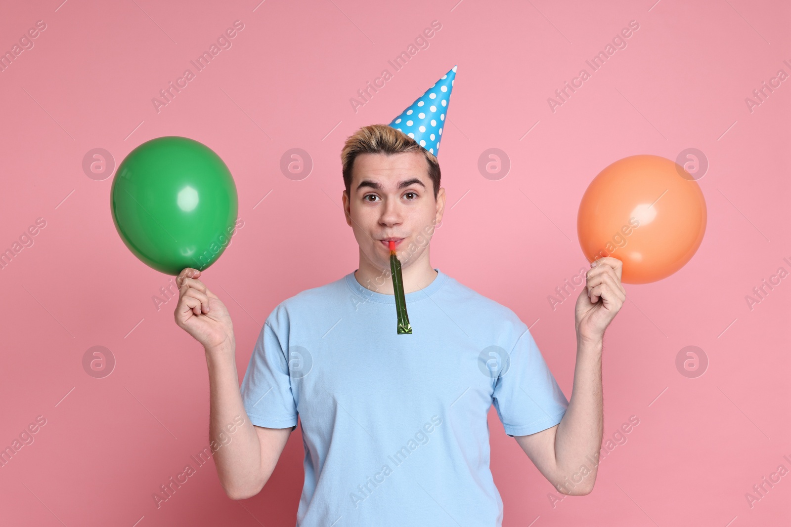 Photo of Young man with party hat, balloons and blower on pink background