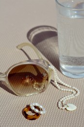 Photo of Stylish sunglasses, glass of water and jewelry on grey surface, closeup