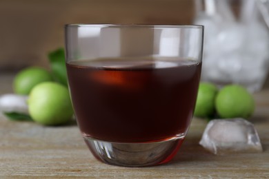 Photo of Delicious liqueur with ice and green walnuts on wooden table, closeup