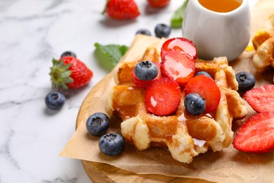 Delicious Belgian waffle with fresh berries and honey on white marble table, closeup