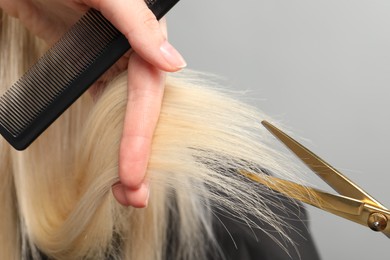 Hairdresser cutting client's hair with scissors on light grey background, closeup