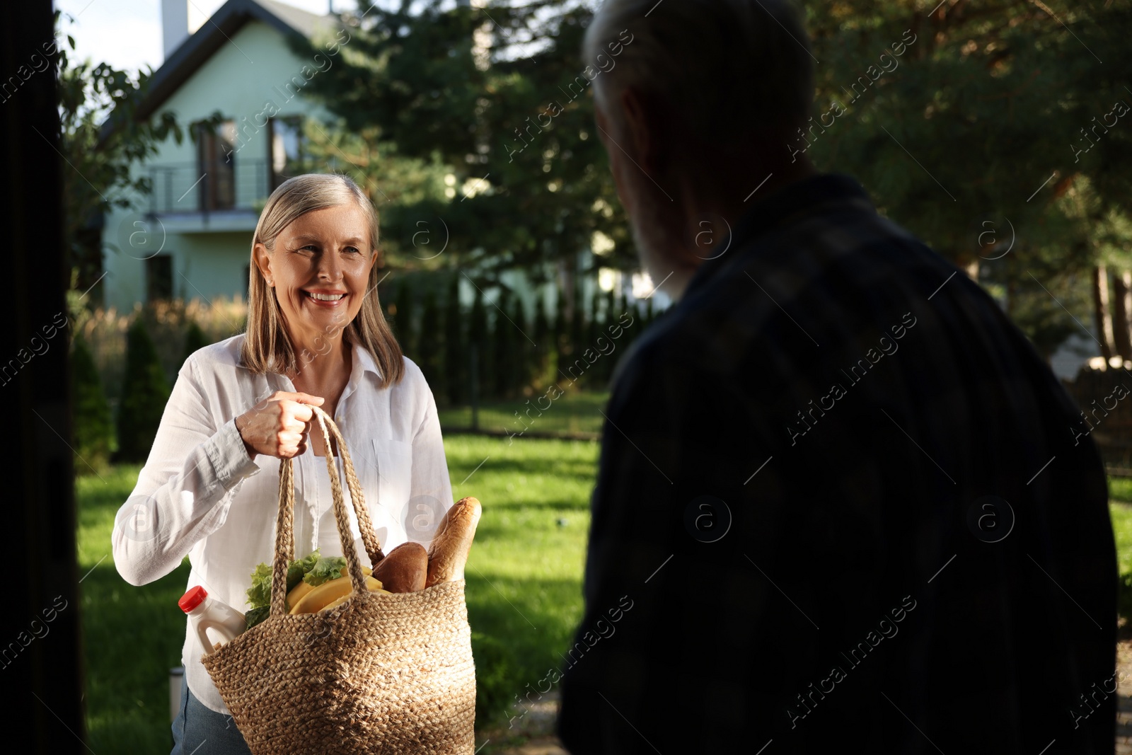 Photo of Helping neighbours. Senior woman with bag of products visiting man outdoors