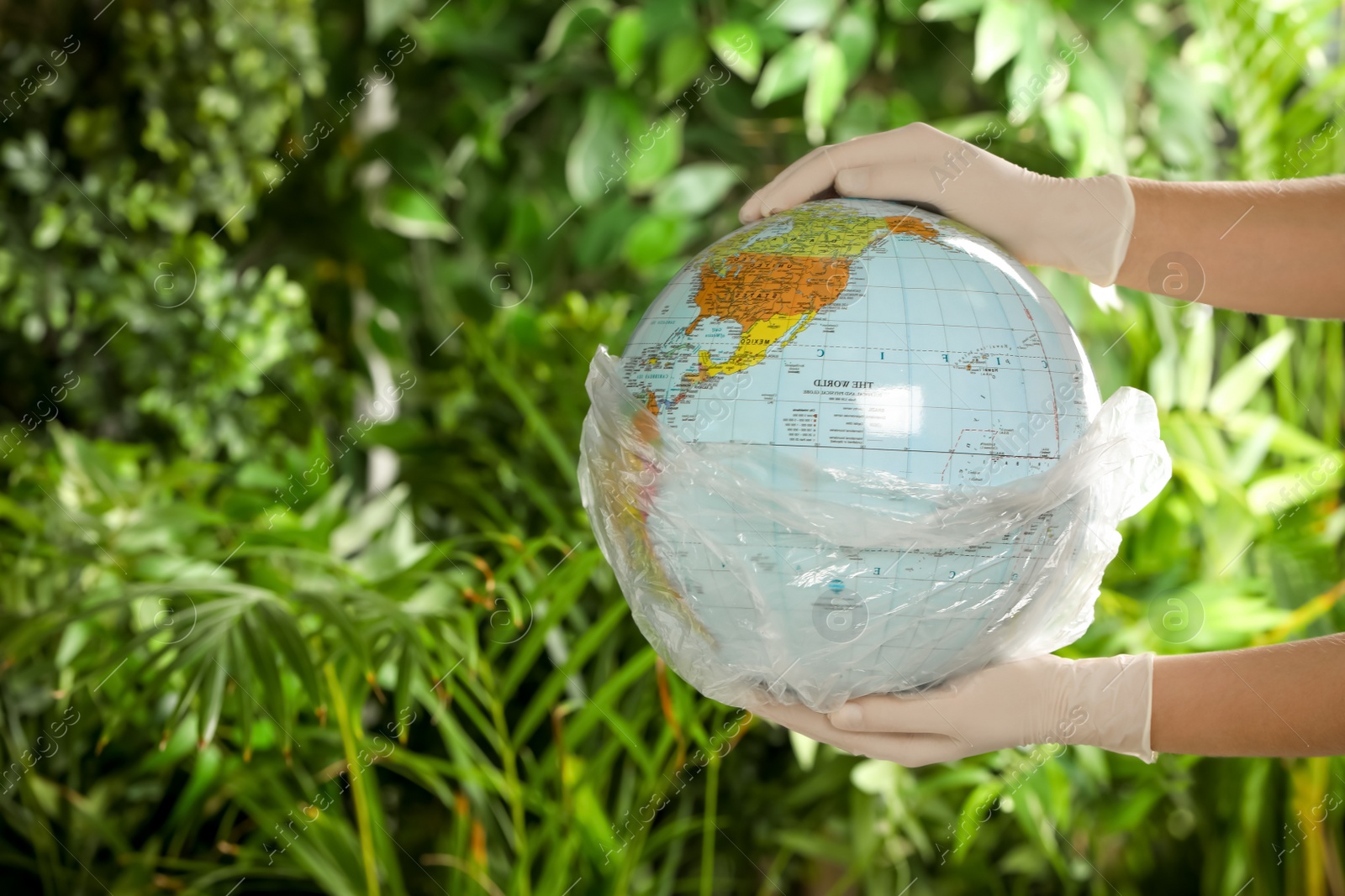 Photo of Woman holding globe in plastic bag against green leaves, closeup. Space for text. Environmental conservation