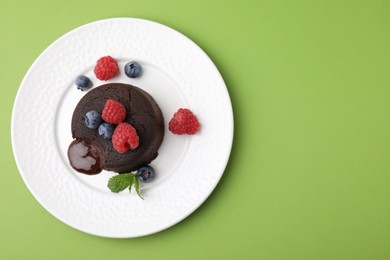 Plate with delicious chocolate fondant, berries and mint on light green table, top view. Space for text