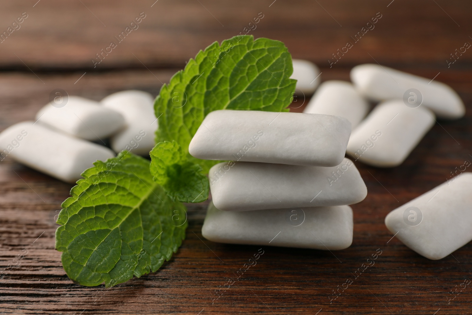 Photo of Tasty white chewing gums and mint leaves on wooden table, closeup