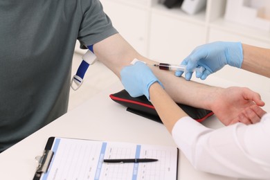 Photo of Doctor taking blood sample from patient with syringe at white table in hospital, closeup