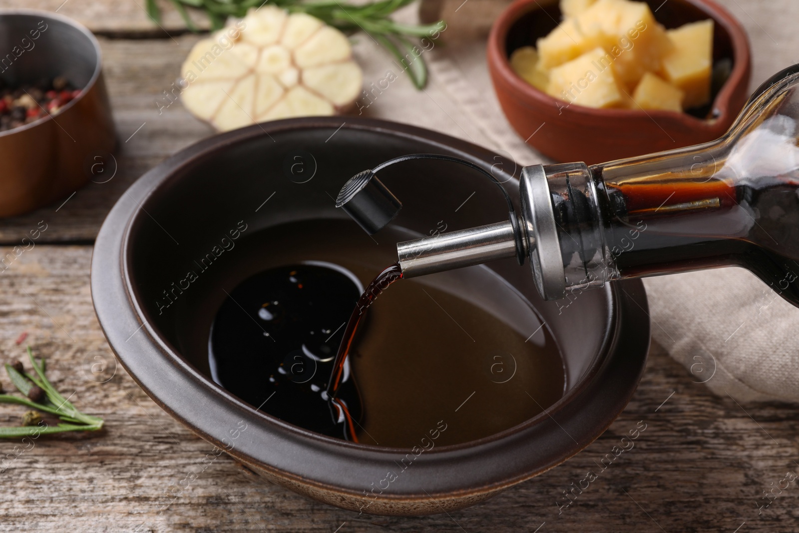 Photo of Pouring balsamic vinegar into bowl with oil on wooden table, closeup