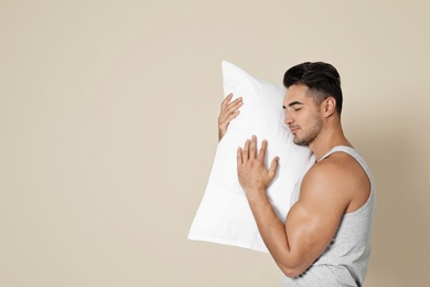 Young man with soft pillow on color background