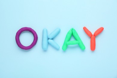Photo of Word Okay made of colorful plasticine on light blue background, top view