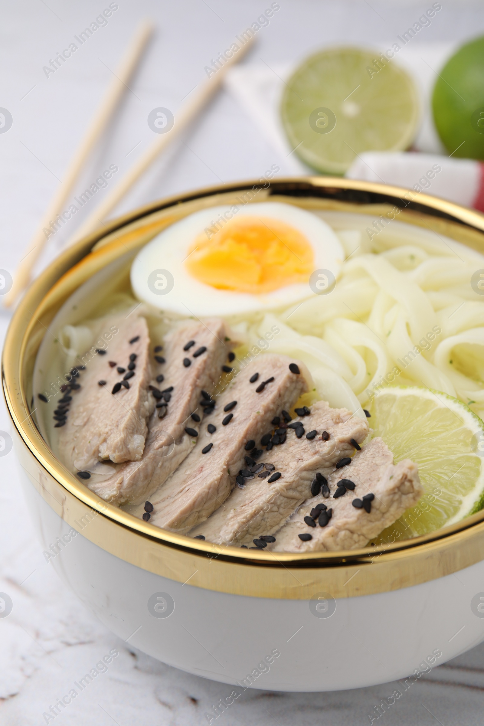 Photo of Bowl of delicious rice noodle soup with meat and egg on white textured table, closeup
