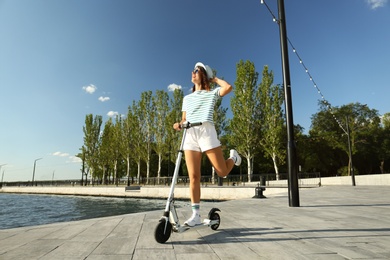Young woman riding modern kick scooter along waterfront