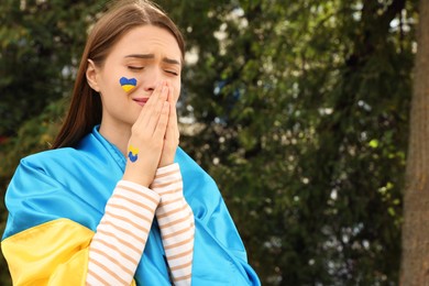 Photo of Emotional young Ukrainian woman with clasped hands outdoors, space for text
