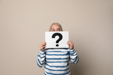 Photo of Mature woman holding paper with question mark on beige background