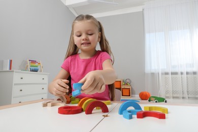 Photo of Motor skills development. Girl playing with colorful wooden arcs at white table in kindergarten, low angle view