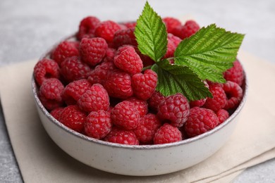 Photo of Bowl of fresh ripe raspberries with green leaves on table, closeup