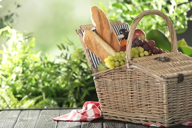 Photo of Wicker picnic basket with different products on table against blurred background, space for text