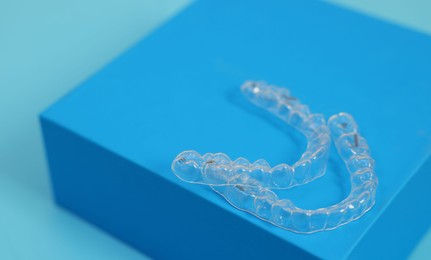 Photo of Transparent dental aligners on light blue background, closeup. Space for text