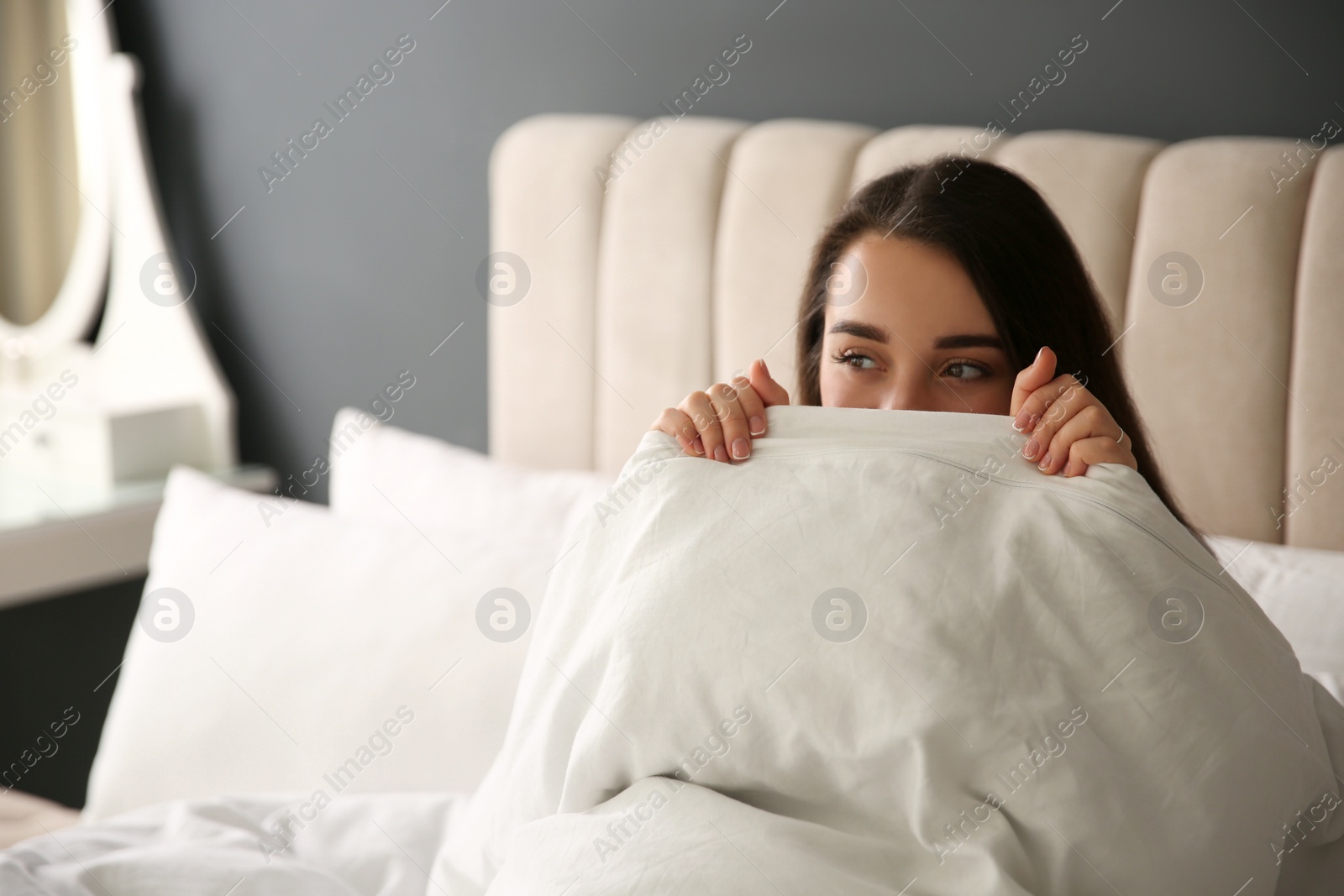 Photo of Beautiful young woman wrapped with soft blanket relaxing on bed at home