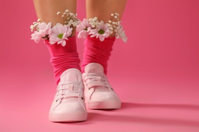 Woman with beautiful tender flowers in socks on pink background, closeup. Space for text