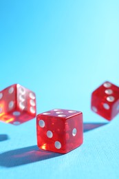 Photo of Three red game dices falling on light blue background, closeup