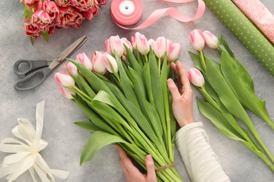 Photo of Woman making bouquet of beautiful fresh tulips at grey table, top view