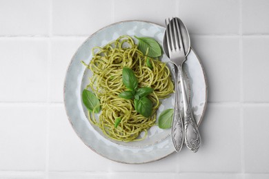 Photo of Delicious pasta with pesto sauce and basil served on white tiled table, flat lay