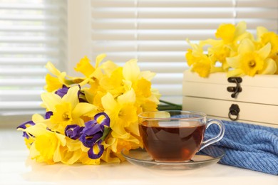 Photo of Cup of aromatic tea, beautiful yellow daffodil and iris flowers on windowsill. Space for text