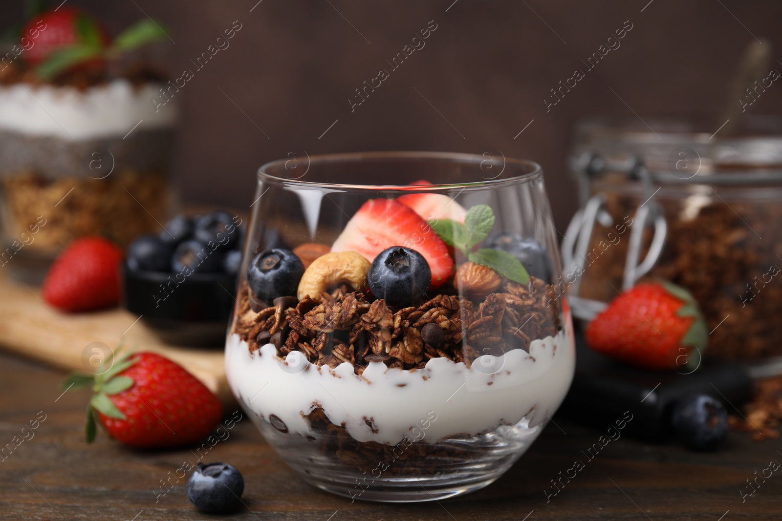 Photo of Tasty granola with berries, nuts and yogurt in glass on wooden table, closeup