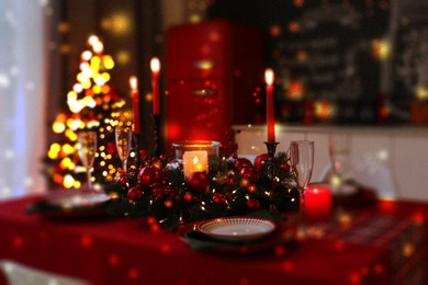 Christmas table setting for festive dinner, bokeh effect. Candles, wreath, plates and glasses on table indoors