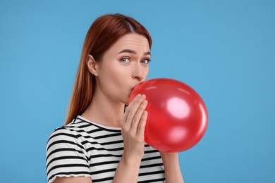 Woman inflating red balloon on light blue background