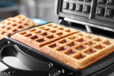 Modern iron with tasty Belgian waffles on table, closeup